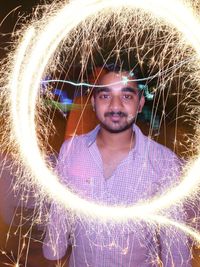 Portrait of young man standing against illuminated light at night