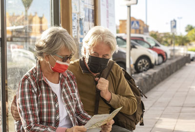 Senior couple wearing mask looking at map in city