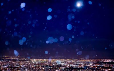 Snowfall over illuminated cityscape against sky at night