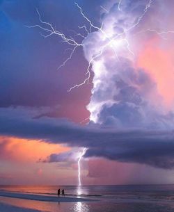 Silhouette couple standing at beach against forked lightning in sky at sunset