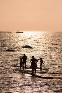 Silhouette people on beach against sky during sunset