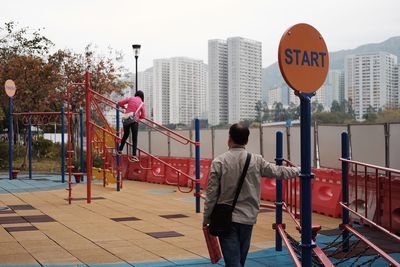 Rear view of man looking at girl playing on jungle gym