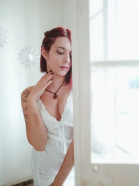 Portrait of young woman standing against window