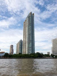 Modern buildings by river against sky in city