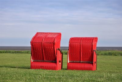 Red hooded chairs on field against sky