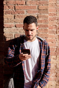 Young man using mobile phone against brick wall