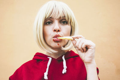 Woman eating french fries in front of peach wall