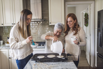 Senior woman and adult granddaughters cooking pancakes for breakfast