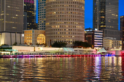 Illuminated buildings by river in city at night