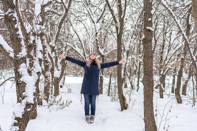 Full length of woman wearing warm clothing standing on snow in forest