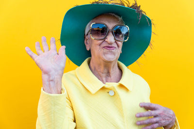 Portrait of smiling senior woman gesturing against yellow background