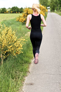 Full length rear view of woman running on road by grassy field