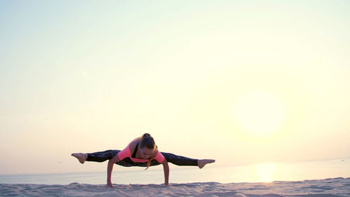 Healthy, young beautiful woman meditating, stretching, practicing yoga on the sea beach, at sunrise