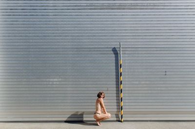 Side view of woman sitting against closed wall