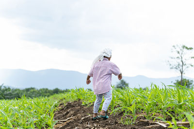 Rear view of boy walking on field against sky