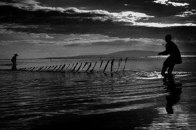 Silhouette man standing at beach against sky