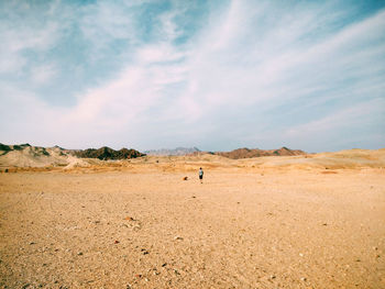 Mid distance view of boy exploring desert against cloudy sky