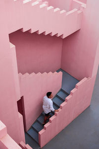 Young latin man goes down the stairs of a pink building