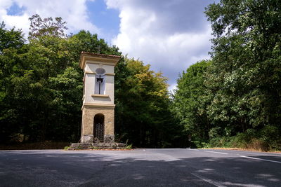 Road by trees and building against sky