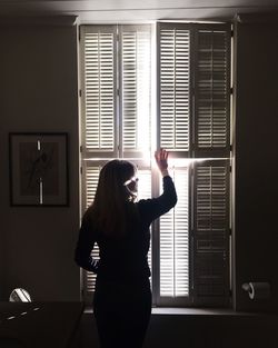 Rear view of woman holding window shutter at home