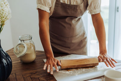 Midsection of a woman in apron rolling dough for cookies at table