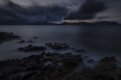 Scenic view of sea and mountains against sky at dusk