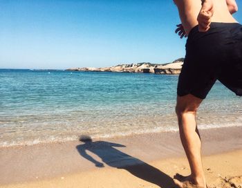 Low section of man playing on beach against clear sky