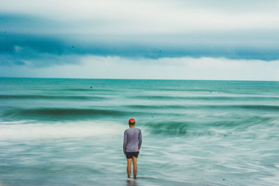 Rear view of man standing on beach against sky