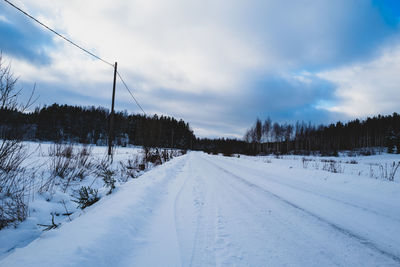 Snow covered road amidst trees against sky during winter