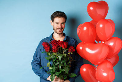 Portrait of man with red balloons against blue background