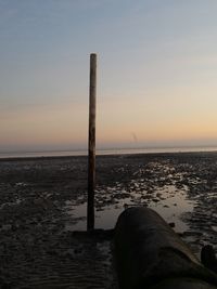 Wooden post in sea against sky during sunset