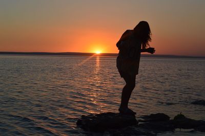 Silhouette woman standing on rock against sea during sunset