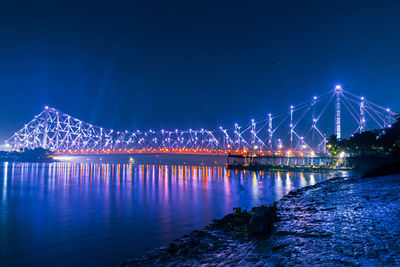 Illuminated bridge over river against sky at night