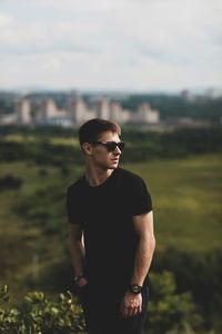 Young man wearing sunglasses standing on field against sky