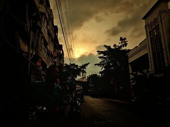 Street amidst buildings against sky at sunset