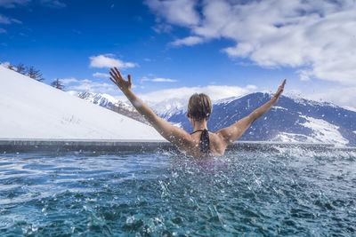 Rear view of woman with arms raised enjoying in infinity pool against mountains