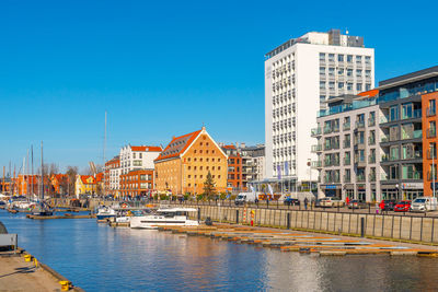 Buildings by river against clear blue sky