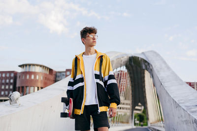 Caucasian teenager standing with a skateboard in the middle of the bridge in the city