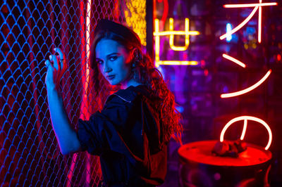 Portrait of young woman standing against illuminated city at night