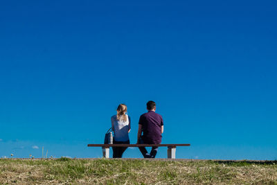 Couple sitting on bench against clear blue sky