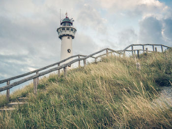 Lighthouse by building against sky