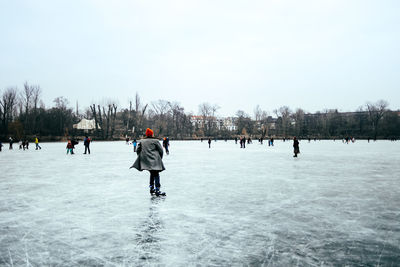 People on frozen lake against sky during winter