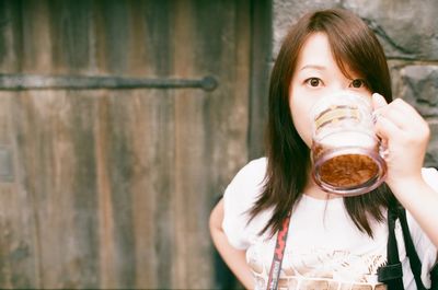 Portrait of woman drinking beer against wooden door
