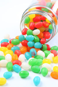 Multi colored candies spilling from jar against white background