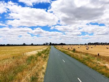 Road by agricultural field against sky