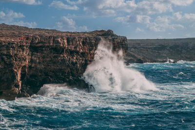 Sea waves splashing on rocks against sky