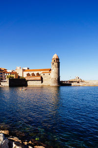 Historic building by sea against clear blue sky