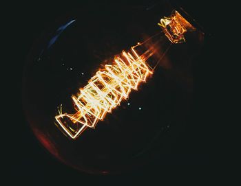 Close-up of illuminated light bulb over black background
