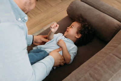 Midsection of father playing with son on sofa