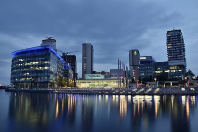 Illuminated buildings by river against sky